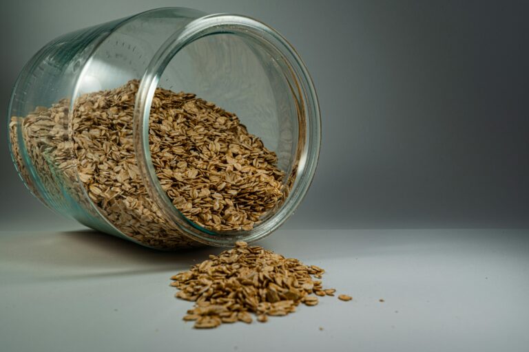 A glass jar spilling rolled oats onto a plain surface, showcasing a rustic breakfast ingredient.